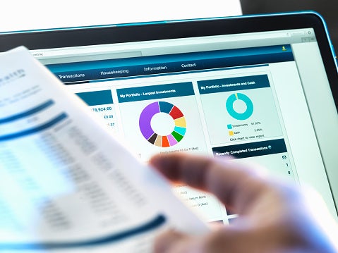 Computer screen showing investment graphs and a hand holding a piece of paper