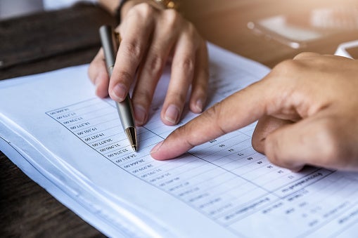 Two hands, one with a pen pointing to a sheet with financial information.