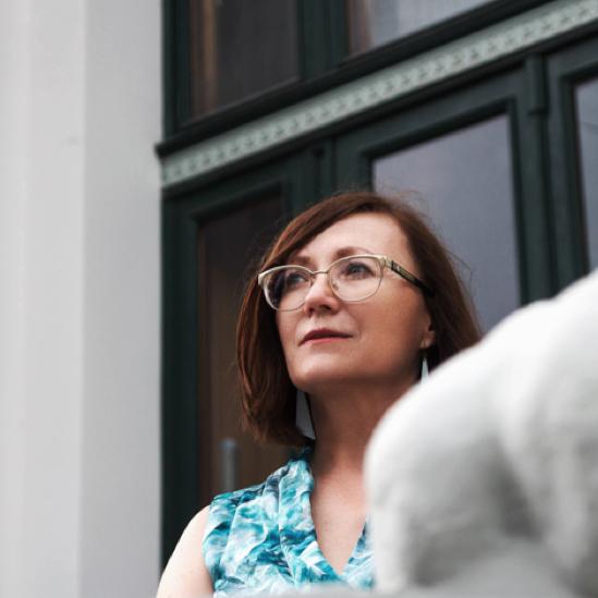 Brunette woman in plastic rimmed glasses & blue shirt looking off into the distance