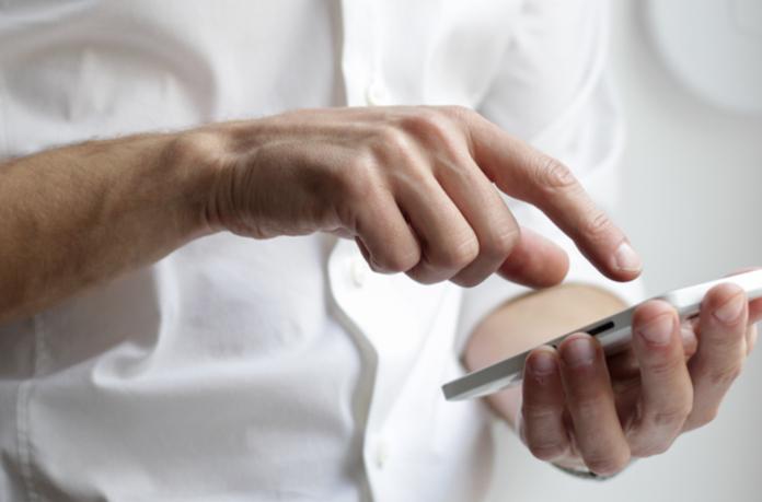 Man in white button up shirt touches iphone with his right index finger.