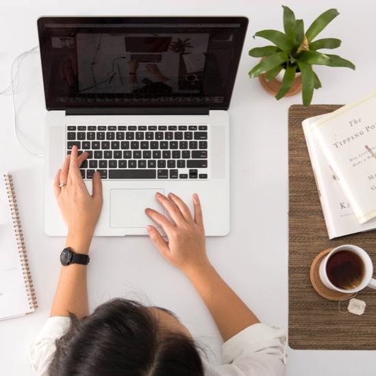 A dark-haired woman typing on her laptop with a cup of coffee to her right
