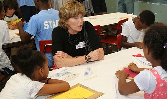 CSB employee sitting at a table talking with 3 children who are doing drawings