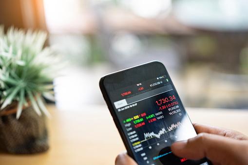 A hand holding a phone looking at stocks