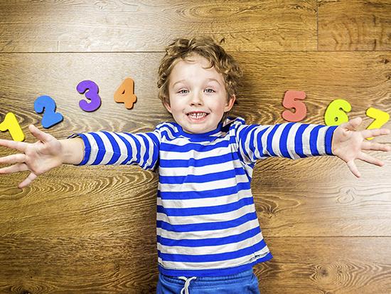 Kid lying on floor with arms spread out with numbers one through seven spread around him