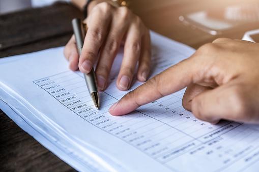 Two hands, one with a pen pointing to a sheet with financial information.