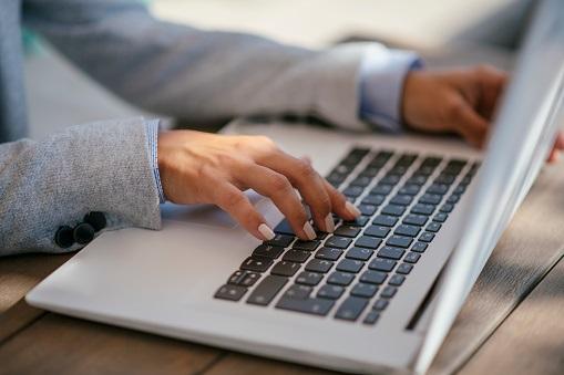 A woman's hands typing on a laptop keyboard